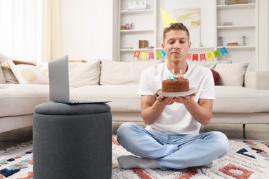 Photo of Birthday celebration. Man with cake making wish while having video call via laptop at home