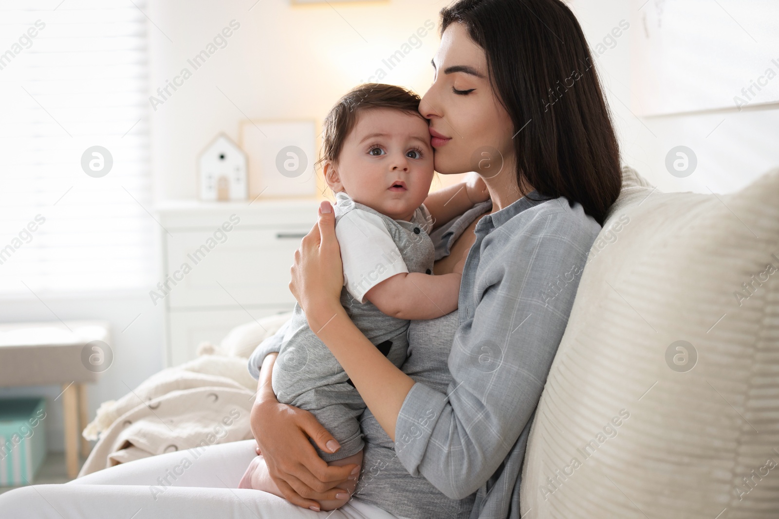 Photo of Mother kissing her cute baby on sofa at home. Space for text