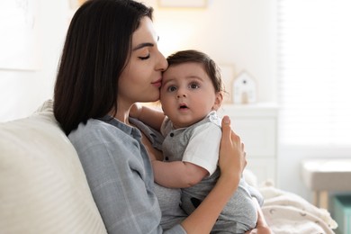 Photo of Mother kissing her cute baby on sofa at home