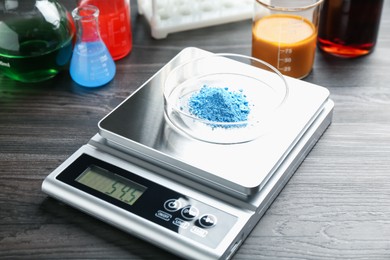 Photo of Laboratory scale with Petri dish of sample on wooden table, closeup