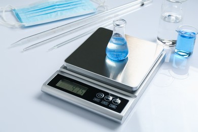 Photo of Scale with flask of sample and other laboratory equipment on white background