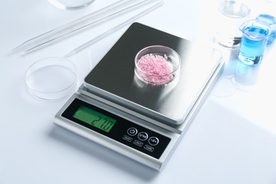 Photo of Scale with Petri dish of sample and other laboratory equipment on white background, closeup