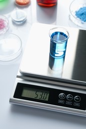 Photo of Scale with beaker of sample and other laboratory equipment on white background, closeup