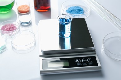 Photo of Scale with beaker of sample and other laboratory equipment on white background, closeup