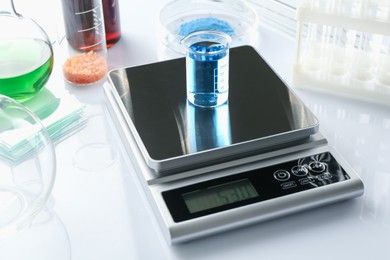 Photo of Scale with beaker of sample and other laboratory equipment on white background, closeup