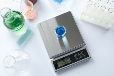 Photo of Scale with beaker of sample and other laboratory equipment on white background, flat lay