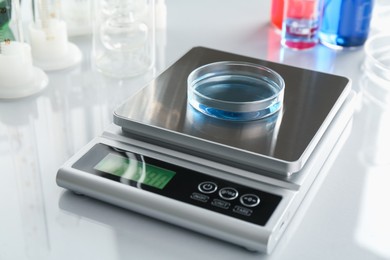 Photo of Scale with Petri dish of sample and other laboratory glassware on white mirror table, closeup