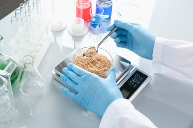 Photo of Scientist weighing Petri dish with sample on scales at white mirror table, closeup
