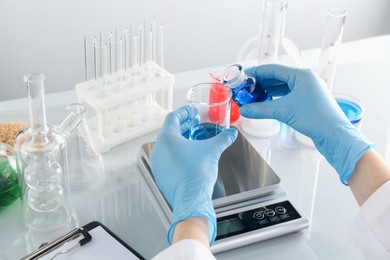 Photo of Scientist working with samples and scales at white mirror table in laboratory, closeup