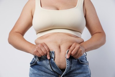 Photo of Overweight woman trying to put on tight jeans against light background, closeup