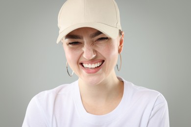 Photo of Smiling woman in stylish baseball hat on grey background, closeup