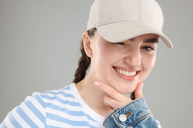 Photo of Happy woman in stylish baseball hat on grey background, closeup