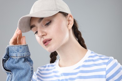 Photo of Beautiful woman in stylish baseball hat on grey background, closeup