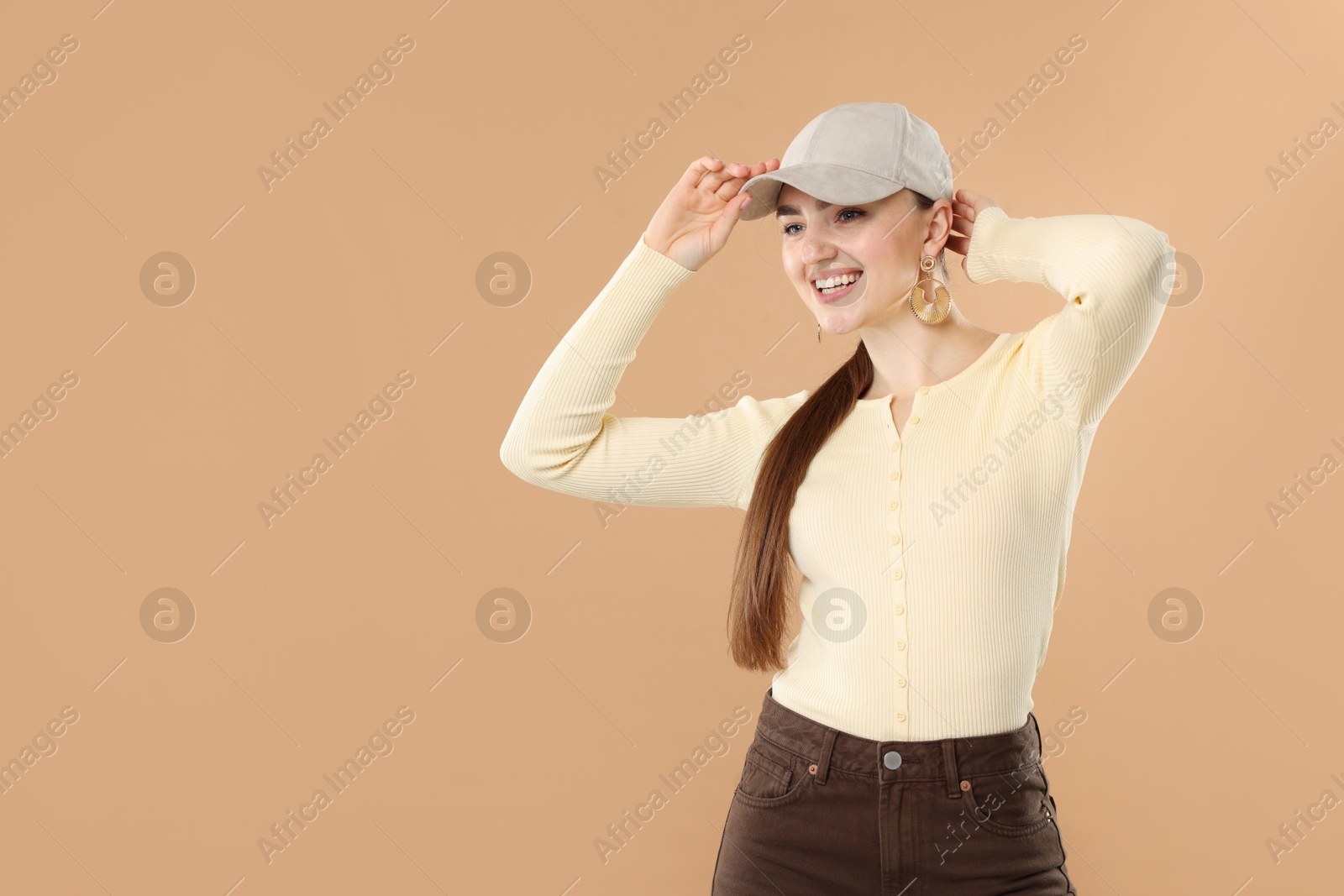 Photo of Smiling woman in stylish baseball hat on beige background. Space for text