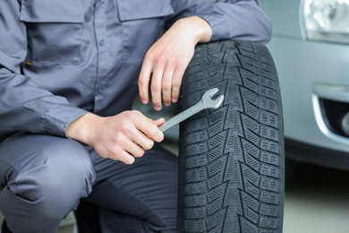 Photo of Mechanic with wrench and tire at car service, closeup