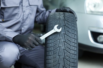 Photo of Mechanic with wrench and tire at car service, closeup