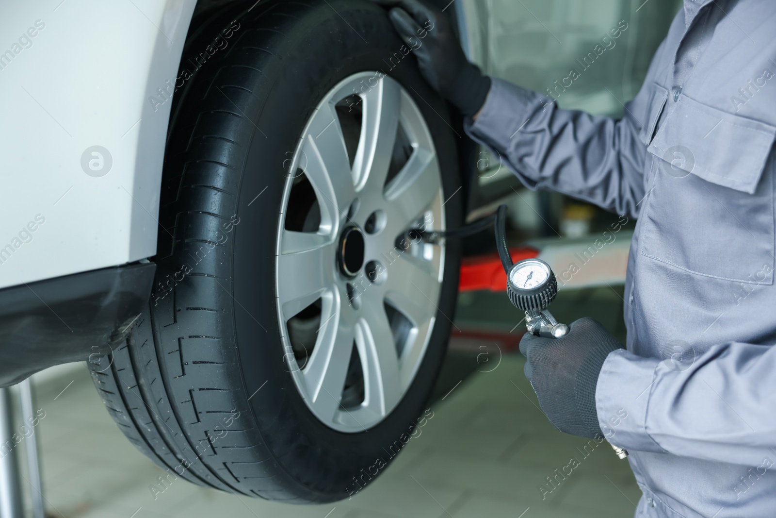 Professional mechanic with tire inflation gun near lifted car in garage Photo of Professional mechanic with tire inflation gun near lifted car in garage