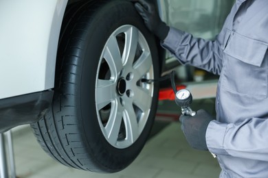 Photo of Professional mechanic with tire inflation gun near lifted car in garage