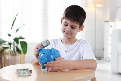 Photo of Boy putting pocket money into piggybank at table indoors