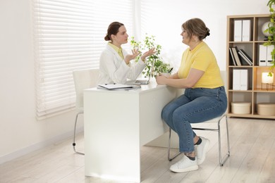 Photo of Weight loss. Nutritionist consulting overweight woman at white desk in clinic