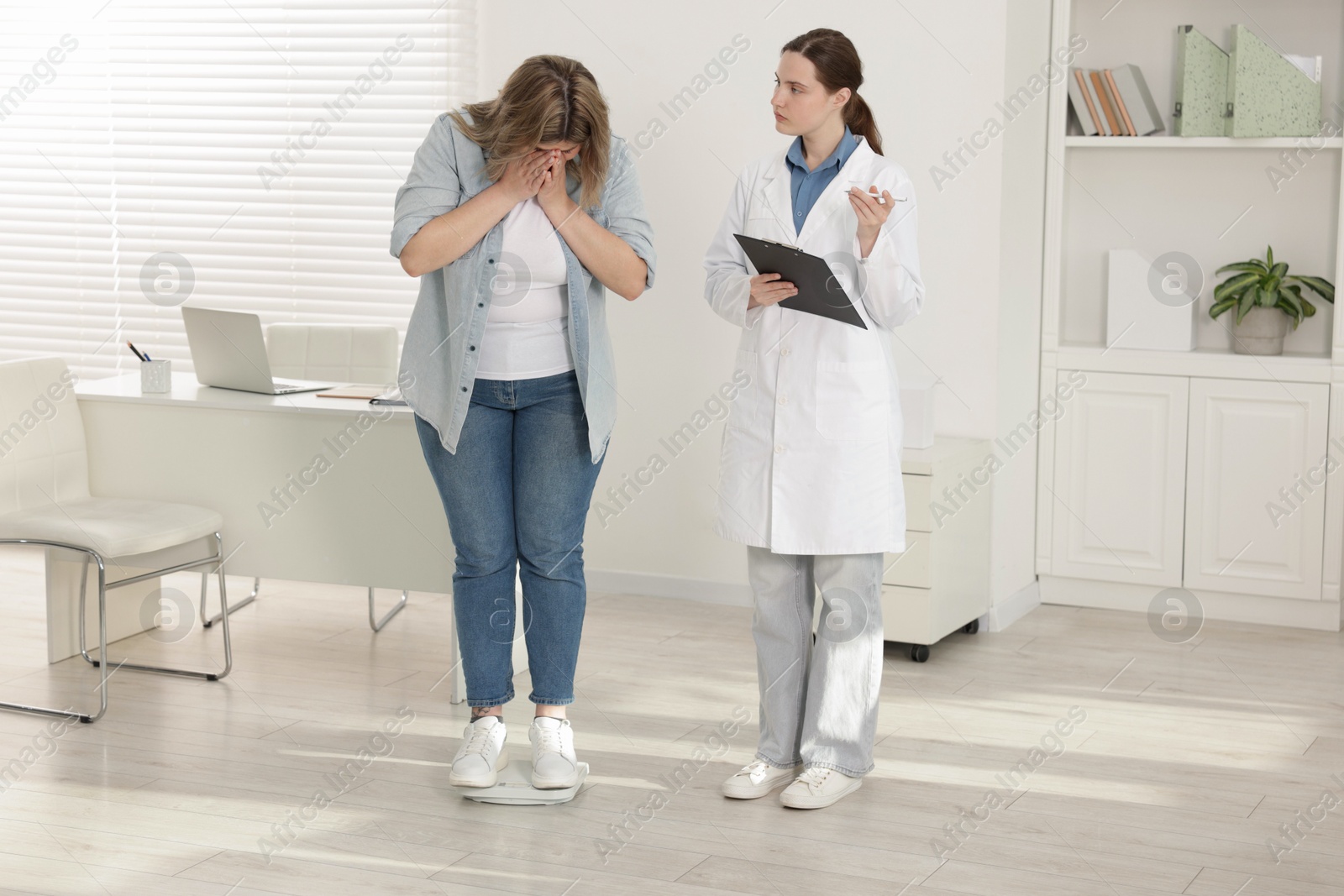 Photo of Weight loss. Shocked overweight woman standing on scales during consultation with nutritionist in clinic