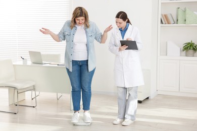 Photo of Weight loss. Upset overweight woman standing on scales during consultation with nutritionist in clinic