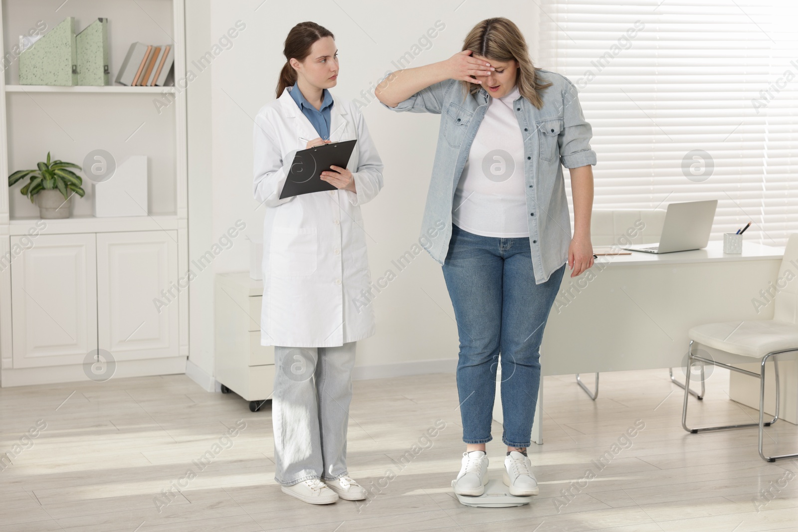 Weight loss. Upset overweight woman standing on scales during consultation with nutritionist in clinic Photo of Weight loss. Upset overweight woman standing on scales during consultation with nutritionist in clinic