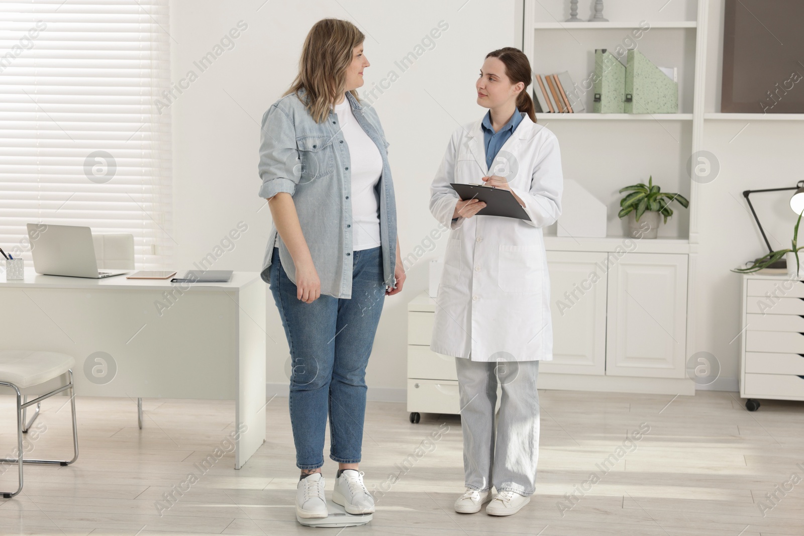 Weight loss. Overweight woman standing on scales during consultation with nutritionist in clinic Photo of Weight loss. Overweight woman standing on scales during consultation with nutritionist in clinic
