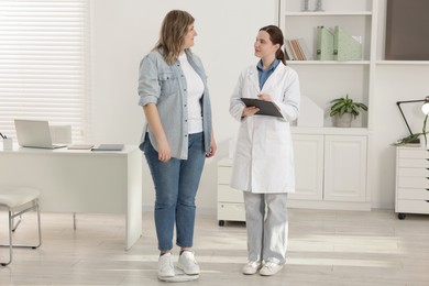 Photo of Weight loss. Overweight woman standing on scales during consultation with nutritionist in clinic