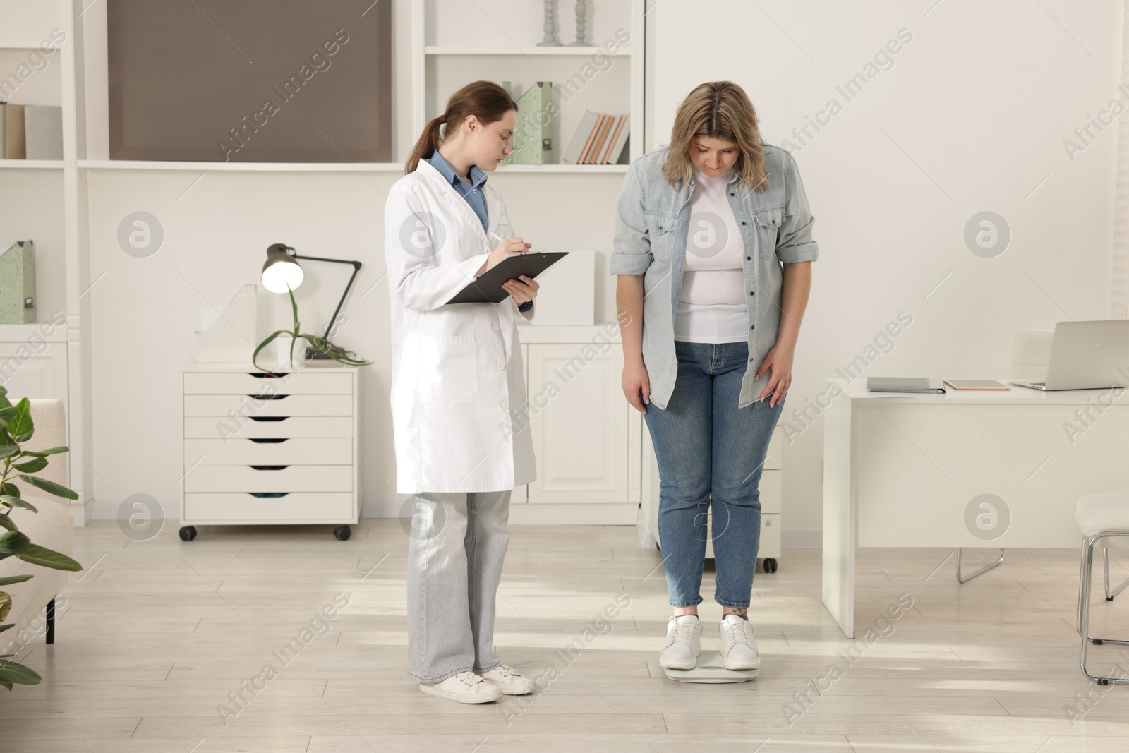 Photo of Weight loss. Overweight woman standing on scales during consultation with nutritionist in clinic