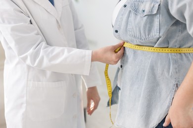 Photo of Weight loss. Nutritionist measuring overweight woman's waist with tape in clinic, closeup