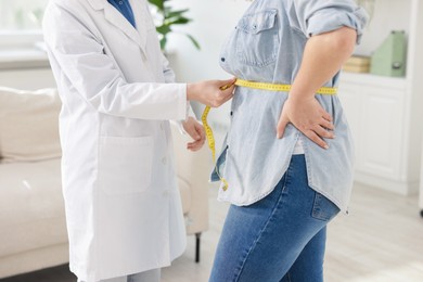Photo of Weight loss. Nutritionist measuring overweight woman's waist with tape in clinic, closeup