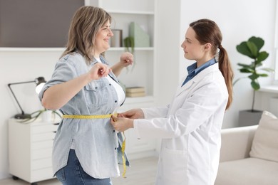 Photo of Weight loss. Nutritionist measuring happy overweight woman's waist with tape in clinic