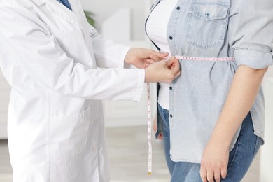 Photo of Weight loss. Nutritionist measuring overweight woman's waist with tape in clinic, closeup