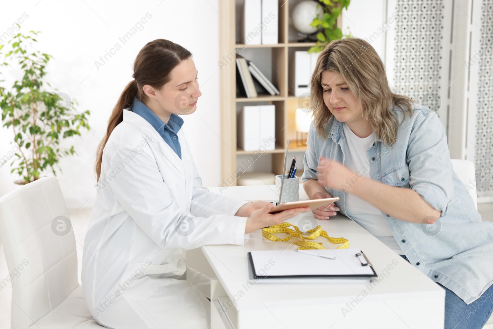 Weight loss. Nutritionist consulting overweight woman at white desk in clinic Photo of Weight loss. Nutritionist consulting overweight woman at white desk in clinic