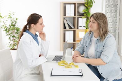 Photo of Weight loss. Nutritionist consulting overweight woman at white desk in clinic