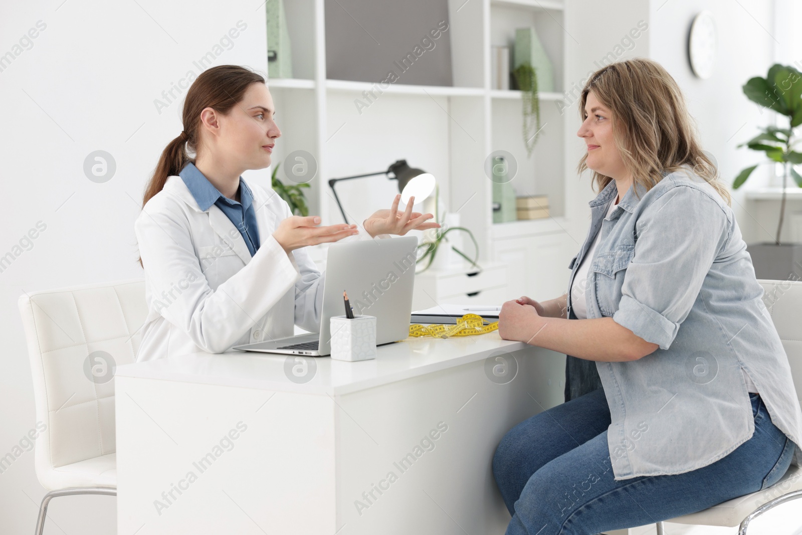 Photo of Weight loss. Nutritionist consulting overweight woman at white desk in clinic