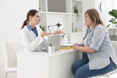 Photo of Weight loss. Nutritionist consulting overweight woman at white desk in clinic