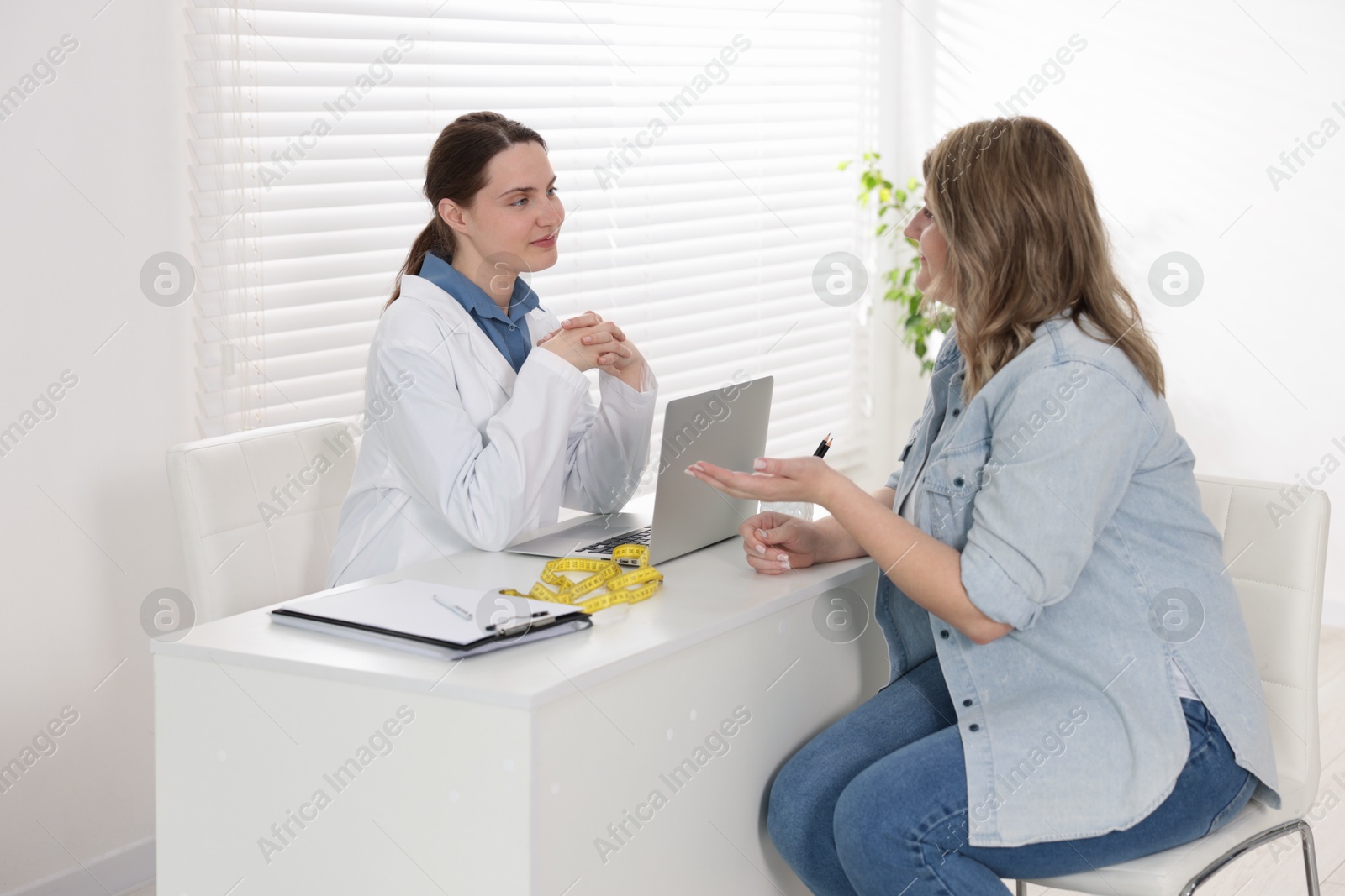 Photo of Weight loss. Nutritionist consulting overweight woman at white desk in clinic