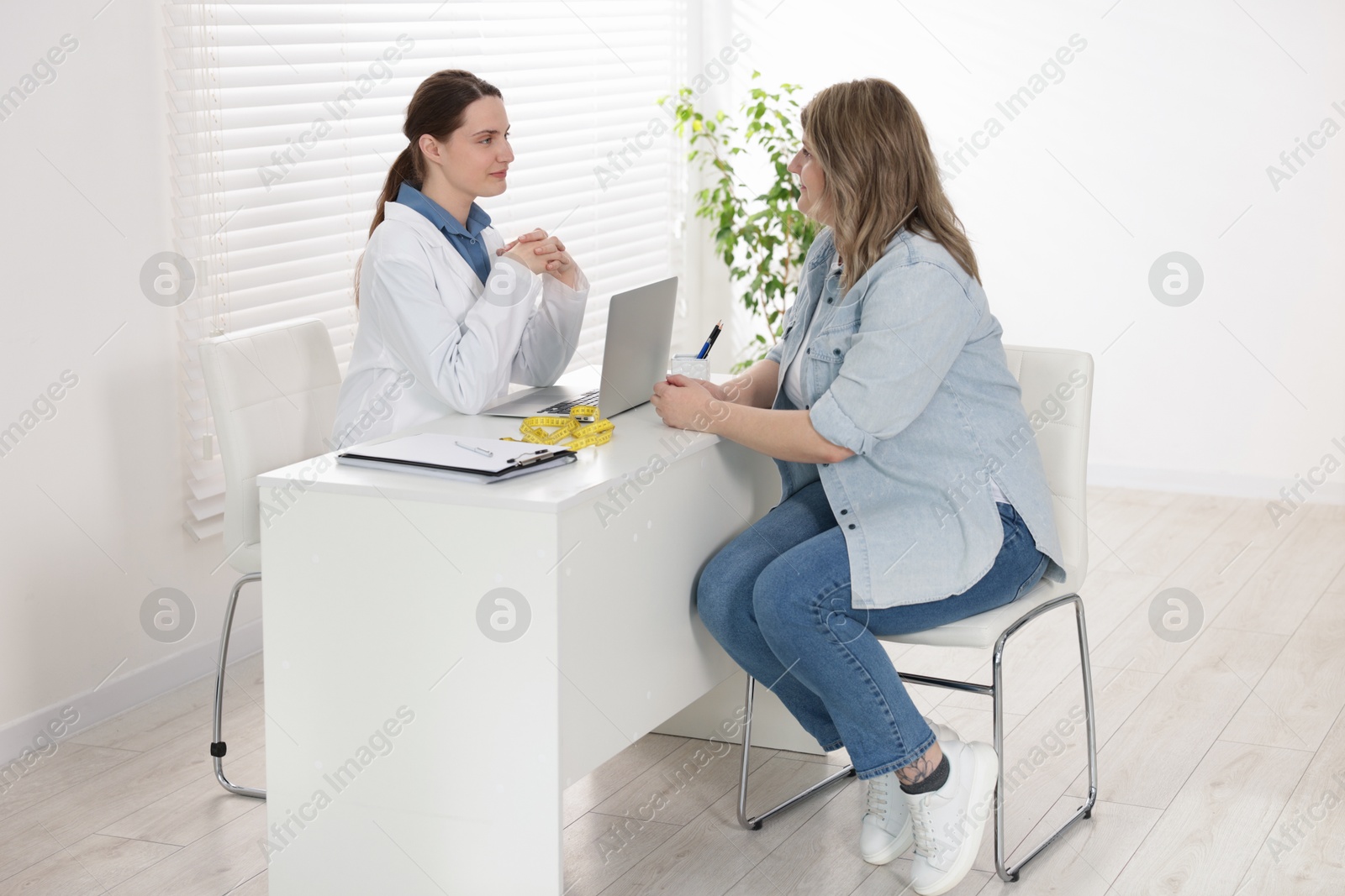 Photo of Weight loss. Nutritionist consulting overweight woman at white desk in clinic