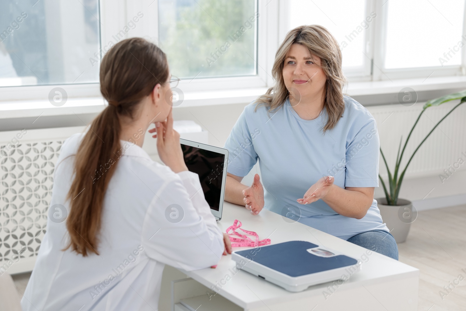 Weight loss. Nutritionist consulting overweight woman at white desk in clinic Photo of Weight loss. Nutritionist consulting overweight woman at white desk in clinic