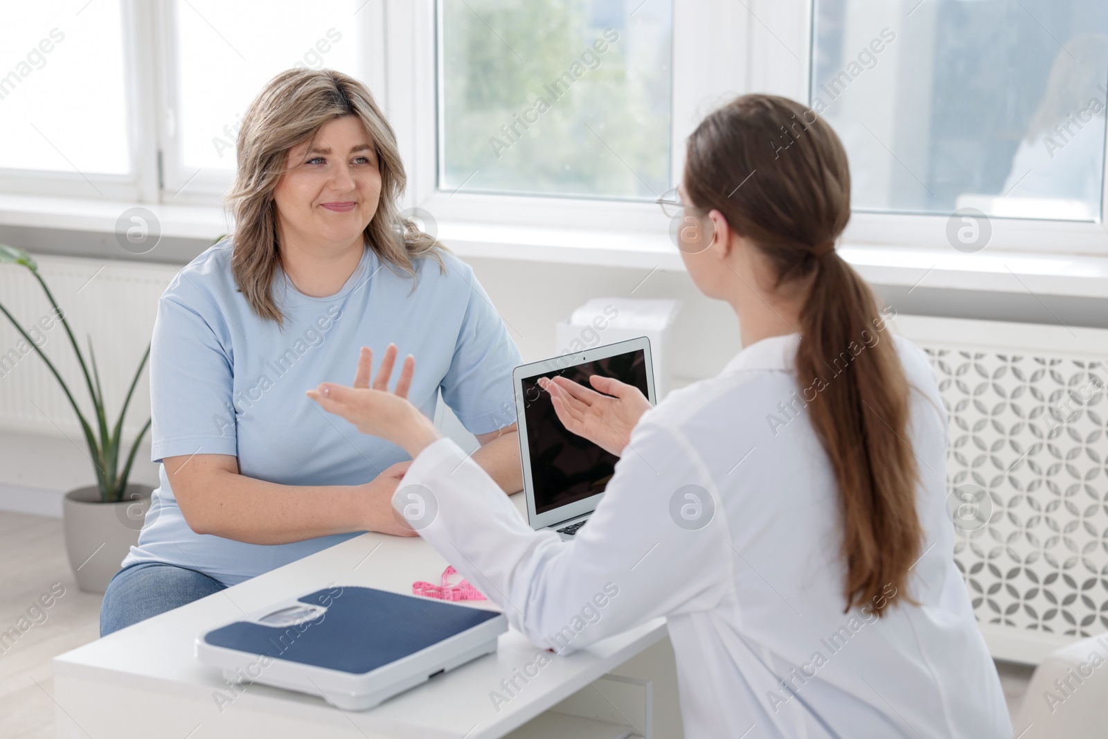 Photo of Weight loss. Nutritionist consulting overweight woman at white desk in clinic