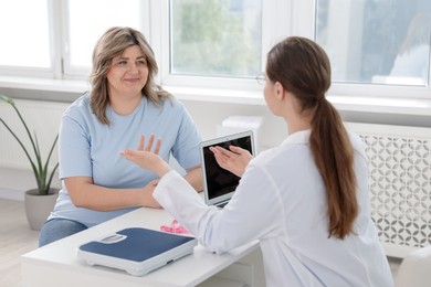 Photo of Weight loss. Nutritionist consulting overweight woman at white desk in clinic