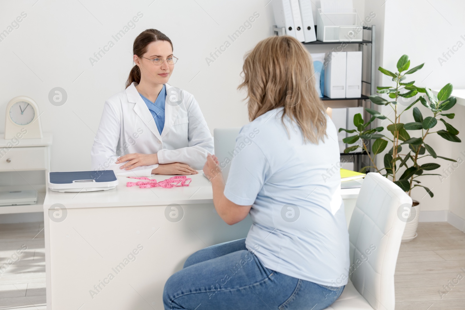 Photo of Weight loss. Nutritionist consulting overweight woman at white desk in clinic