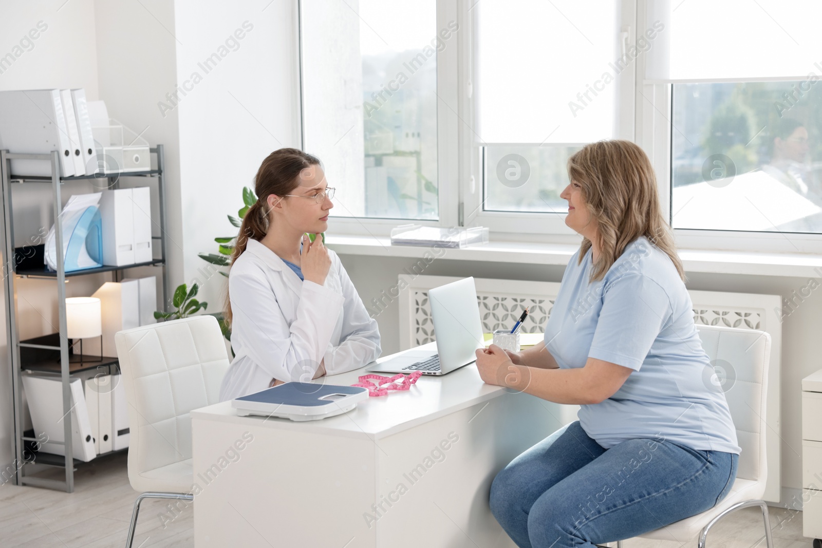 Photo of Weight loss. Nutritionist consulting overweight woman at white desk in clinic