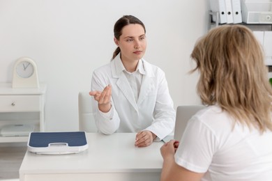 Photo of Weight loss. Nutritionist consulting overweight woman at white desk in clinic