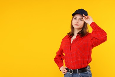 Photo of Young woman wearing stylish black baseball hat on yellow background, space for text