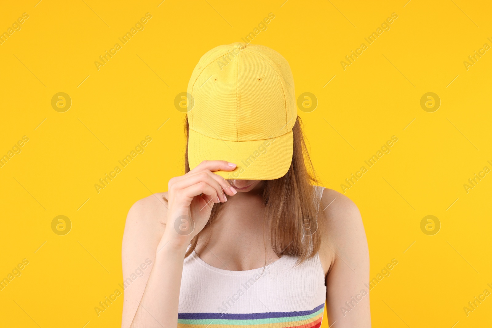 Young woman wearing stylish baseball hat on yellow background Photo of Young woman wearing stylish baseball hat on yellow background
