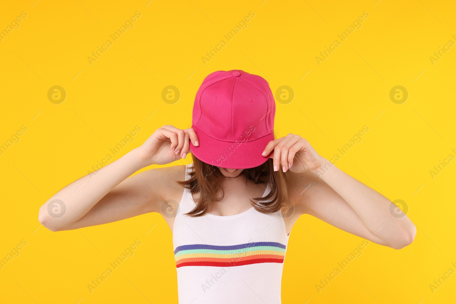 Young woman wearing stylish pink baseball hat on yellow background Photo of Young woman wearing stylish pink baseball hat on yellow background