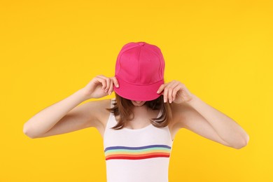 Photo of Young woman wearing stylish pink baseball hat on yellow background
